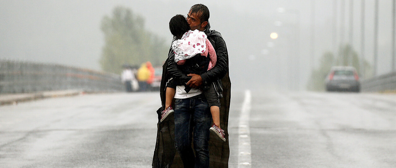 Un refugiado sirio besa a su hija mientras camina bajo la lluvia hacia la frontera de Grecia con Macedonia. 
