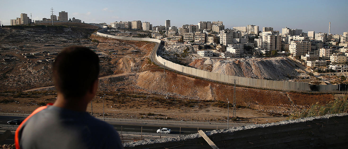 Palestino mirando el campo de personas refugiadas y rodeado por el muro de separación israelí